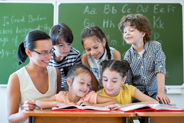 professora ensinando grupo de crianças com livros abertos em sala de aula.