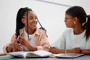 Duas amigas estudando com livros e tablet digital em um projeto de casa.