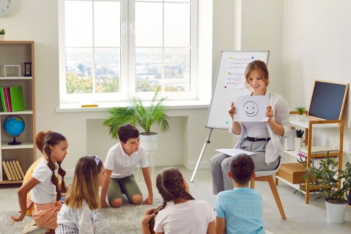 professora ensina competências socioemocionais para crianças, utilizando ilustrações de emoções.