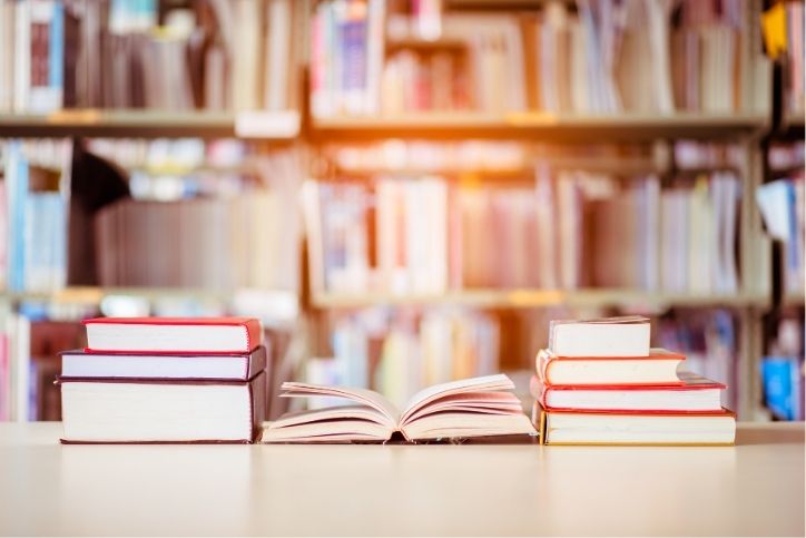 pilhas de livros sobre uma mesa em uma biblioteca.