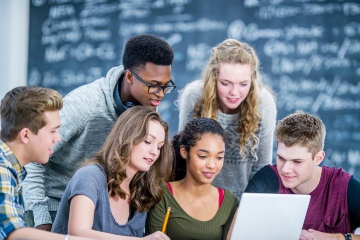 grupo de adolescentes estudando juntos em frente a um laptop na escola.