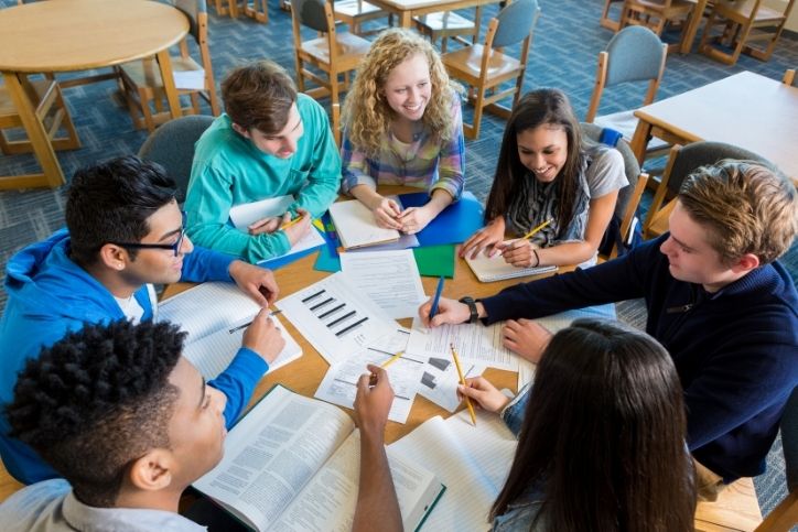 grupo de estudantes reunidos em volta de uma mesa com livros e anotações.