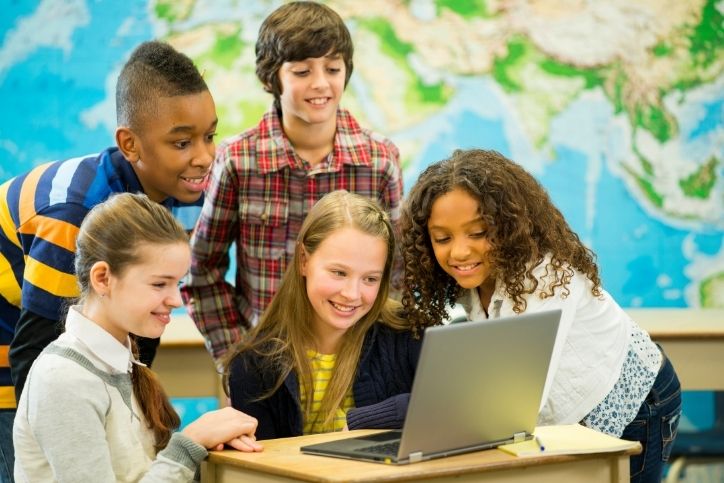 grupo de alunos sorrindo enquanto olham para um notebook na sala de aula.