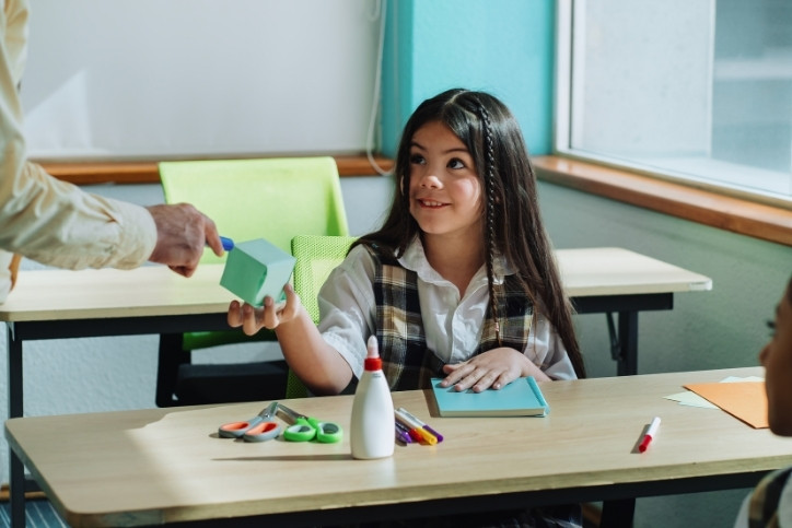 Aluna participando de atividade prática em sala de aula, recebendo material didático como parte da abordagem de construtivismo na educação para estimular o aprendizado ativo.