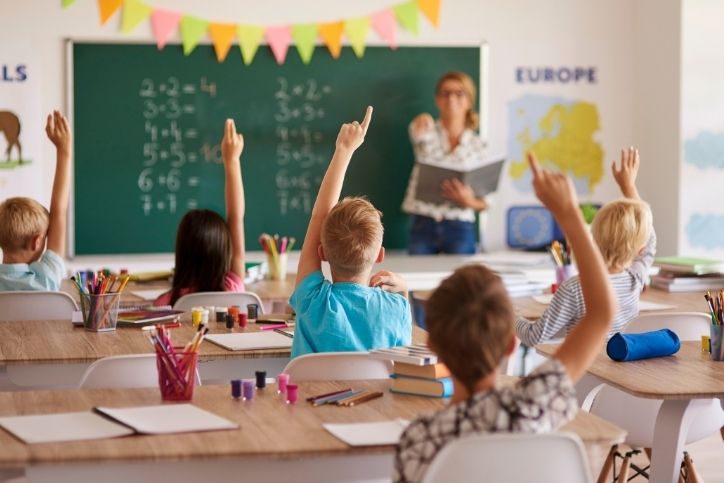 Alunos participando ativamente de aula com professora ao fundo.